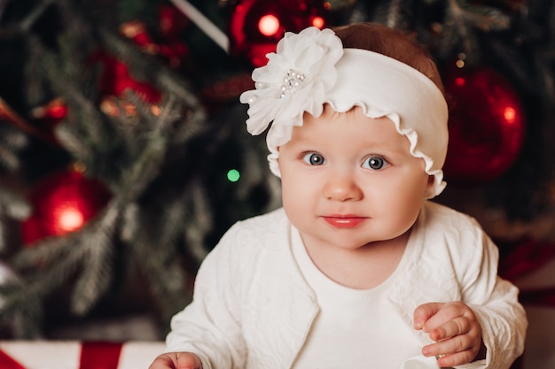 Filho bonito vestido branco posando debaixo da árvore de natal.