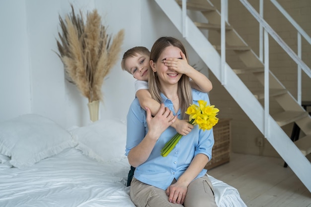 Filho cumprimenta sua mãe com um buquê de flores no quarto em casa