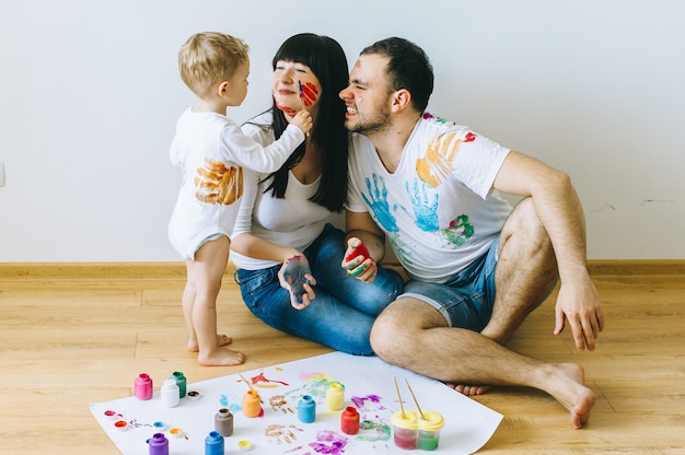 Foto filho de família feliz com os pais e um gato pintando um cartaz e outro com tintas