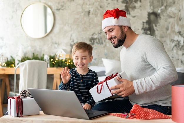 Filho e pai acenando para parentes em videochamada no dia de natal