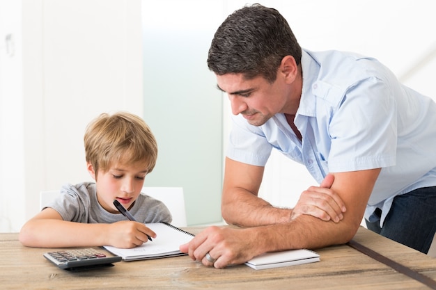 Filho fazendo lição de casa enquanto o pai está de pé