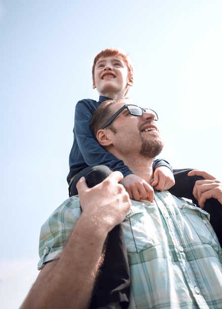 Foto filho feliz senta-se nos ombros de seu pai