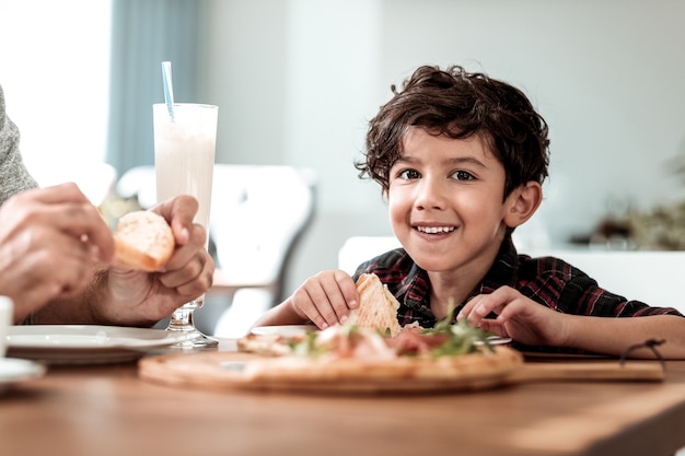 Filho mais novo. Pai barbudo e moreno sentindo-se aliviado enquanto comia pizza com o filho mais novo