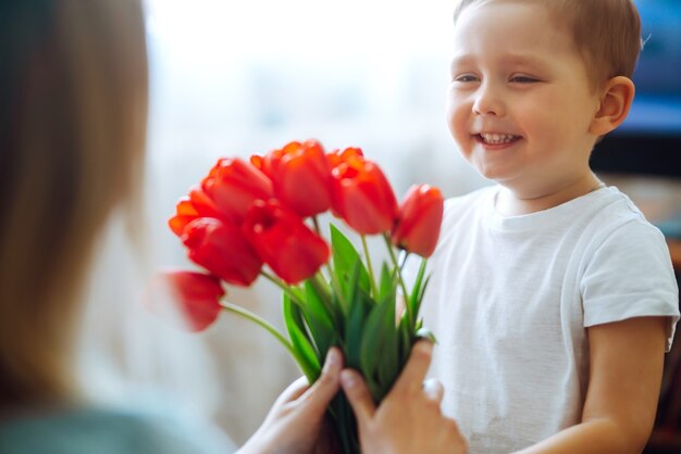 Filho pequeno parabeniza a mãe e dá um buquê de tulipas de flores. Feliz Dia das Mães.