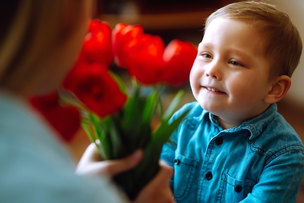 Filho pequeno parabeniza a mãe e dá um buquê de tulipas de flores. Feliz Dia das Mães.