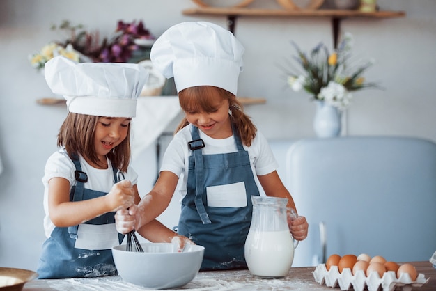 Filhos da família com uniforme branco do chef, preparando a comida na cozinha.