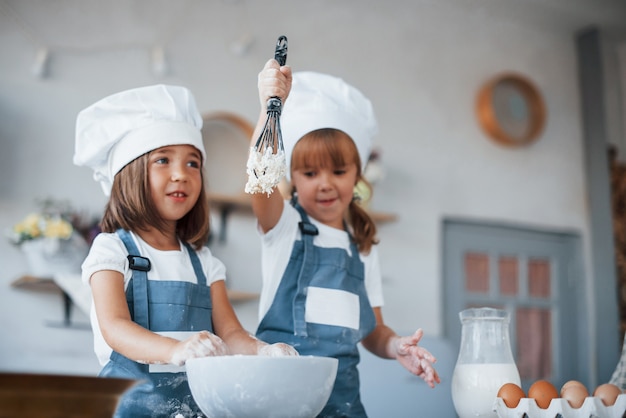 Filhos da família com uniforme branco do chef, preparando a comida na cozinha.