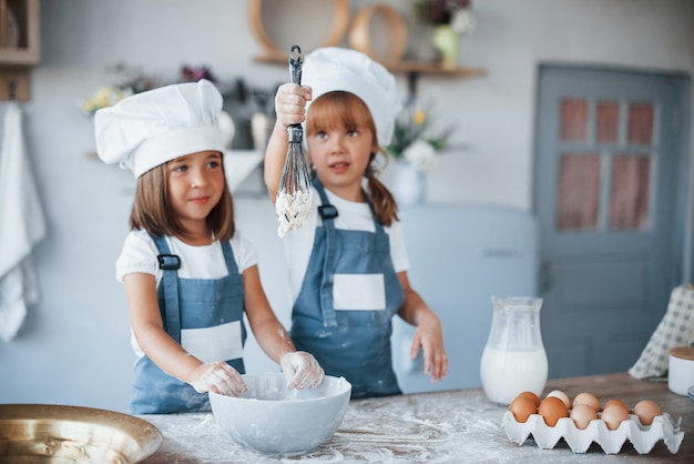 Foto filhos da família com uniforme branco do chef, preparando a comida na cozinha.