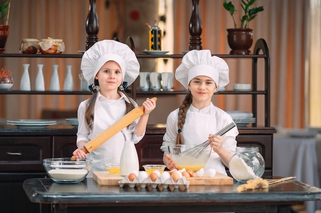 Filhos de garotas engraçadas estão preparando a massa na cozinha.