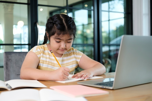 Filhos de menina bonitos e felizes usando o computador portátil, estudando através do sistema de e-learning on-line.