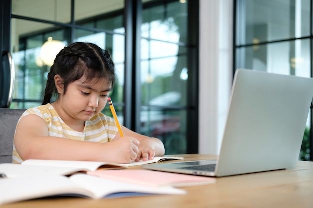 Filhos de menina bonitos e felizes usando o computador portátil, estudando através do sistema de e-learning on-line.