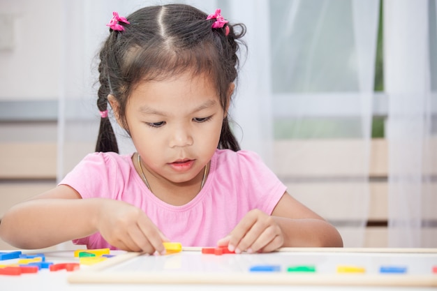 Filhote de garotinha linda que se divirta para jogar e aprender alfabetos magnéticos a bordo no quarto