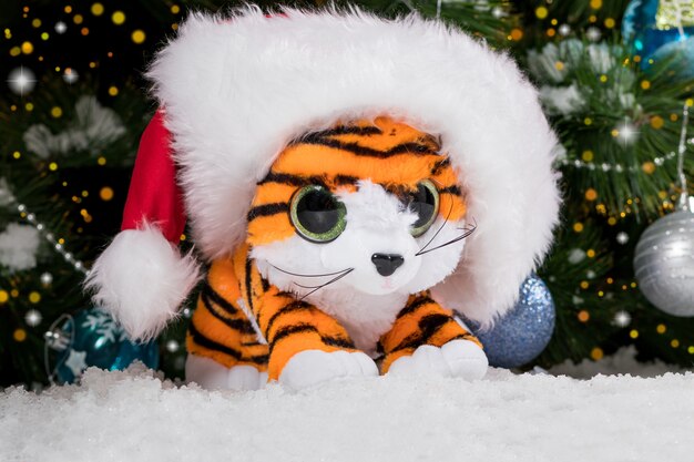 Filhote de tigre de Natal com um chapéu de Papai Noel perto da árvore.