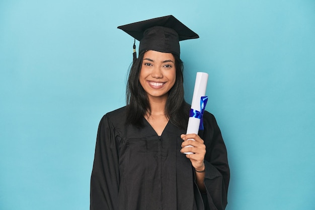 Filipina graduada con diploma en el estudio azul feliz sonriente y alegre