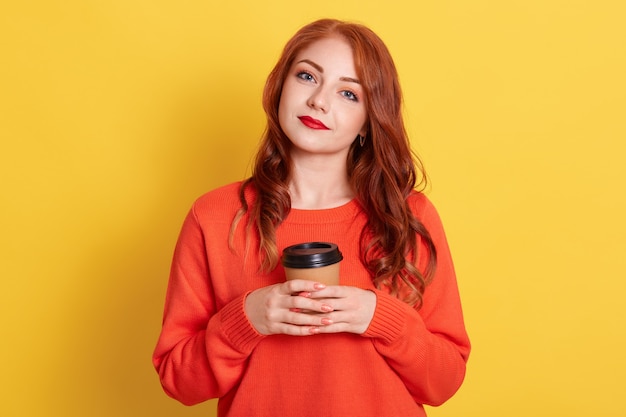 Filmación en interiores de mujer joven con vestidos de pelo rojo en suéter casual naranja