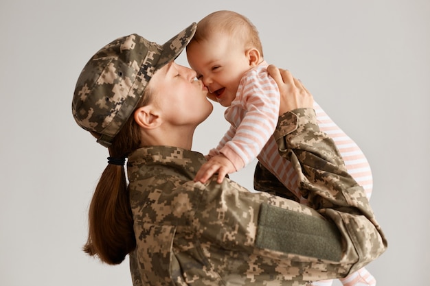 Filmación en interiores de una mujer soldado emocional feliz que regresa a casa del ejército, levantando a su hija pequeña y besándola, saludándola después de regresar a casa de un período de servicio en el extranjero.