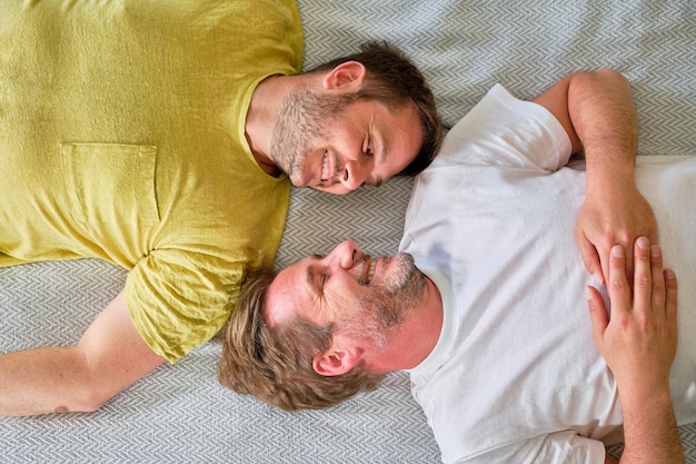 Filmado de cima de um casal gay deitado na cama sorrindo com as cabeças quase juntas olhando um para o outro