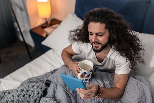 Filme favorito. Vista superior de um jovem positivo sentado com um tablet enquanto assiste a um filme