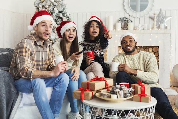 Filme tradicional de Natal. Amigos multiétnicos animados assistindo TV em casa, passando férias juntos, copiando espaço