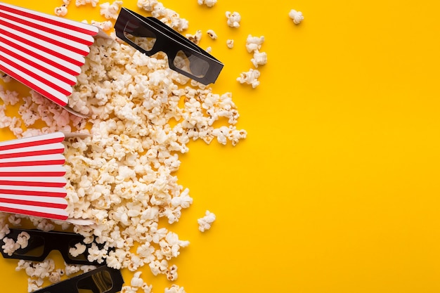 Filmhintergrund, Ansicht von oben. Popcorn und 3D-Brille im klassischen gestreiften Eimer auf gelbem Hintergrund, Kopierraum, Unterhaltungskonzept