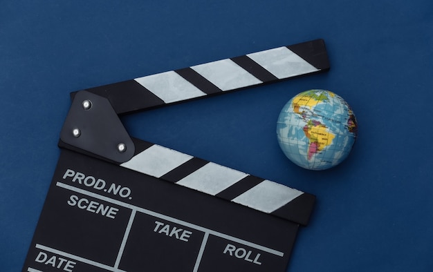 Foto filmklappe mit globus auf klassischem blauem hintergrund. filmemachen, filmproduktion, unterhaltungsindustrie. farbe 2020. ansicht von oben