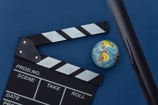Filmklappe mit Globus, Filmband auf klassischem blauem Hintergrund. Filmemachen, Filmproduktion, Unterhaltungsindustrie. Farbe 2020. Ansicht von oben