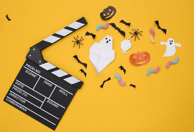 Filmklappe und handgemachtes Halloween-Papierdekor, gummiartige Würmer auf gelbem Hintergrund. Ansicht von oben