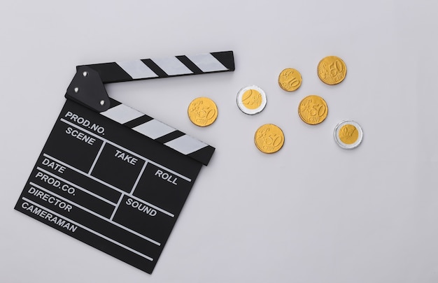 Filmklappe und Münzen auf weißem Hintergrund. Kinogebühren. Filmemachen, Filmproduktion. Ansicht von oben