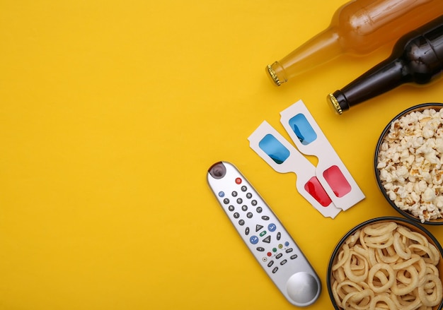 Filmzeit. Snackschalen, Bierflaschen, TV-Fernbedienung, 3D-Brille auf gelbem Hintergrund. Ansicht von oben. Platz kopieren