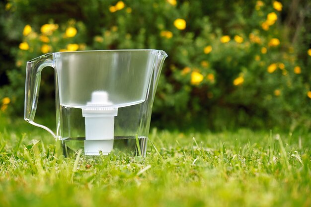 Filtro de agua de pie sobre la hierba verde en el jardín de verano con hermosas flores que crecen en el arbusto en el fondo