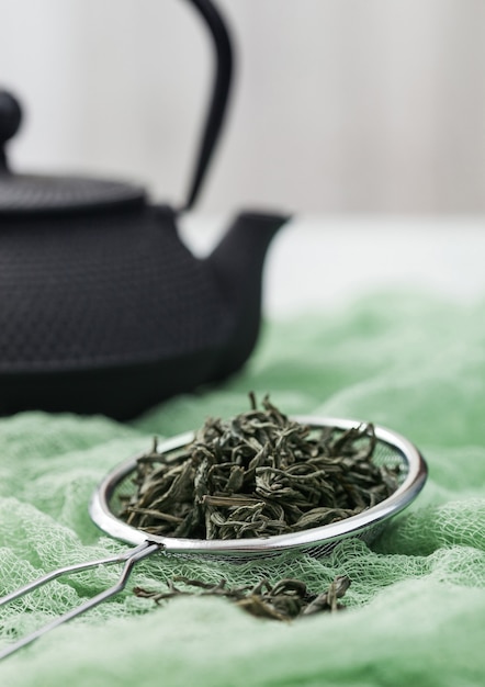 Filtro infusor com chá verde orgânico solto sobre pano verde com bule de ferro preto japonês.