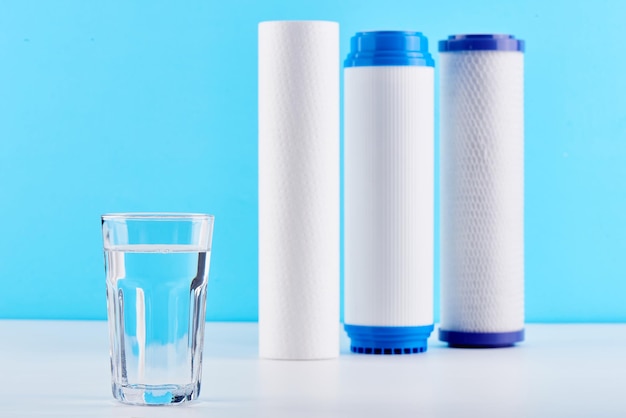 Filtros de agua. Cartuchos de carbón y un vaso sobre un fondo azul blanco. Sistema de filtración doméstico.