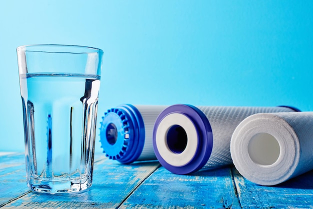 Foto filtros de água. cartuchos de carbono e um copo em um fundo azul. sistema de filtragem doméstico.