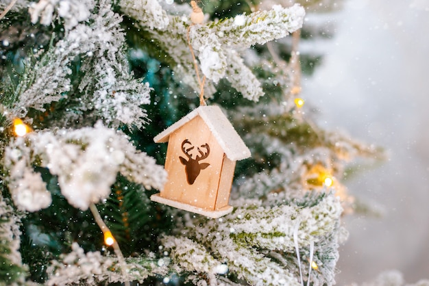 Fim coberto de neve decorado da árvore de natal acima. casa de brinquedo de madeira e guirlanda iluminada com lanternas.