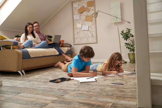 Fim de semana com a família, a jovem mãe e o pai, sentados no sofá e assistindo a um filme no laptop, enquanto