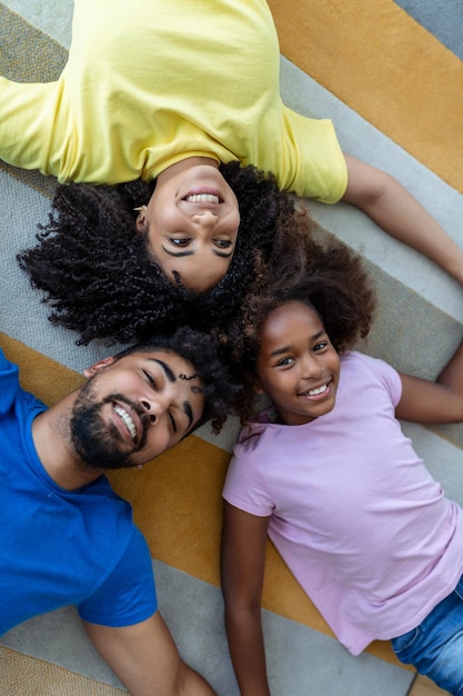 Fim de semana em família sorrindo mãe negra pai e filha deitados na cama juntos relaxando em casa