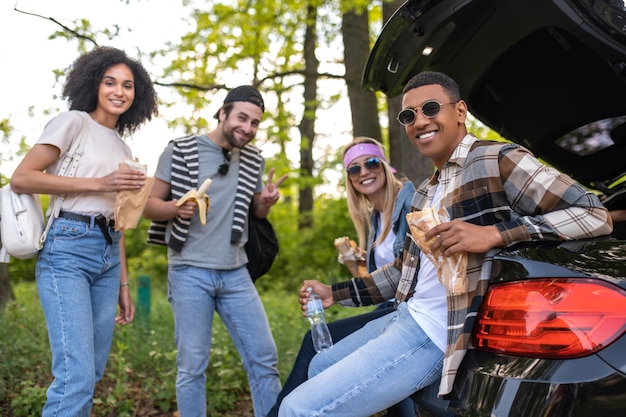 Fin de semana. Amigos comiendo sándwich al aire libre y sintiéndose alegres