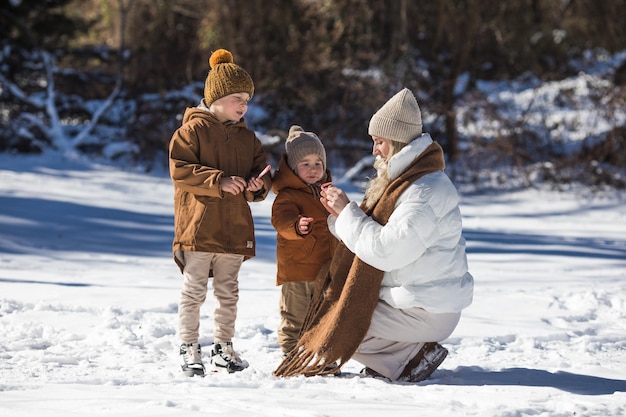 Fin de semana de invierno Madre y dos hijos con ropa de invierno cálida caminando mientras se divierten en el bosque de invierno entre los árboles