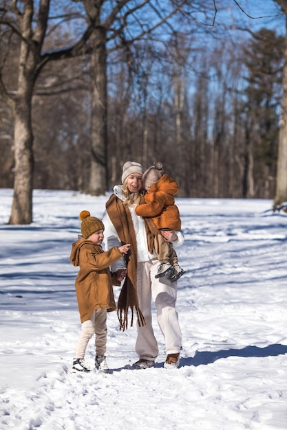 Fin de semana de invierno Madre y dos hijos con ropa de invierno cálida caminando mientras se divierten en el bosque de invierno entre los árboles
