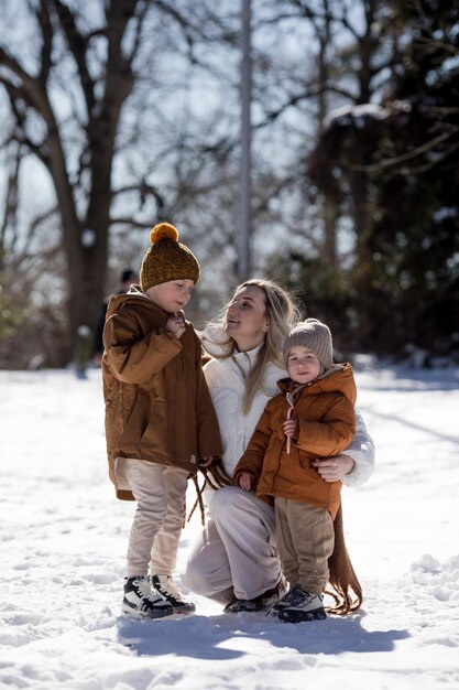 Fin de semana de invierno Madre y dos hijos con ropa de invierno cálida caminando mientras se divierten en el bosque de invierno entre los árboles