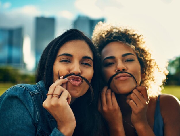 Finalmente encontrei alguém tão louco quanto eu Retrato recortado de duas namoradas jovens e atraentes fazendo um bigode com o cabelo em um parque