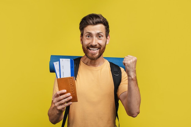 Finalmente vacaciones Emocionado hombre de mediana edad con pasaporte de maleta y boletos exclamando felicidad fondo amarillo