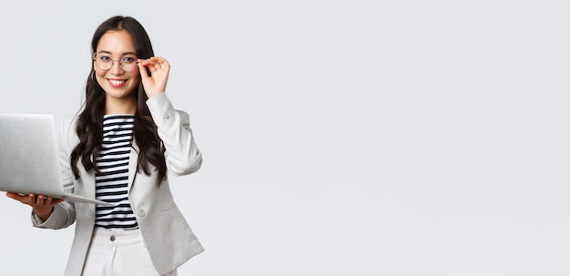 Finanças de negócios e emprego conceito de empreendedores de sucesso feminino confiante sorridente empresária asiática trabalhadora de escritório em terno branco e óculos usando laptop ajuda clientes