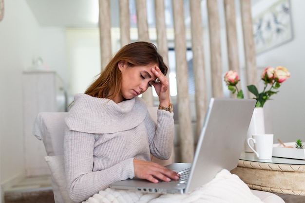 Financista bonita, elegante, atraente, charmosa, triste, chateada de mãos dadas na cabeça, sofrendo de síndrome de dor de cabeça, conceito de saúde sentado em casa trabalhando no laptop