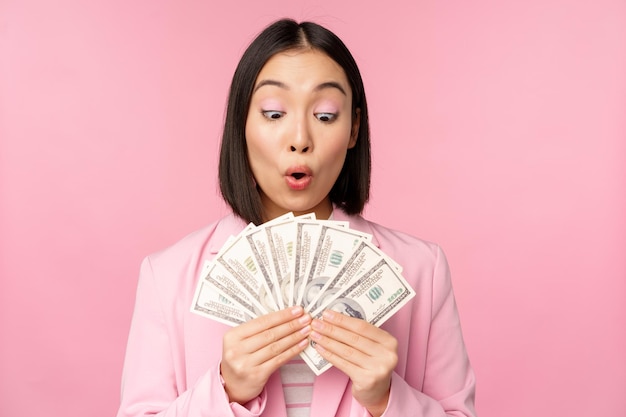 Finanzas microcrédito y concepto de personas Feliz empresaria asiática sonriente mostrando dólares dinero de pie en traje contra fondo rosa