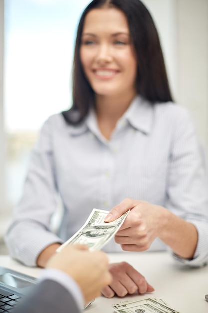 Foto finanzas, moneda, tipo de cambio, negocios y concepto de personas - cierre de la mujer feliz y la mano masculina dando o intercambiando dinero en la oficina