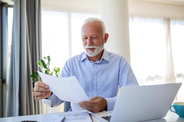 Finanzberater-Geschäftsmann, der seinen Laptop benutzt und etwas Papierkram erledigt, während er am Schreibtisch sitzt und arbeitet