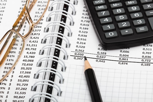 Finanzbericht-Rechner, Bleistift und Brille auf dem Tisch im Büro. Ein Blatt Papier voll