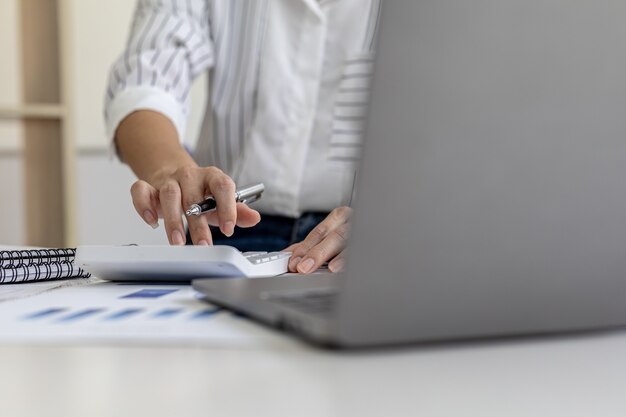 Finanzgeschäftsfrau, die einen weißen taschenrechner drückt, verwendet sie einen taschenrechner, um die zahlen in den finanzdokumenten des unternehmens zu berechnen, die mitarbeiter in der abteilung als besprechungsdokumente erstellen.