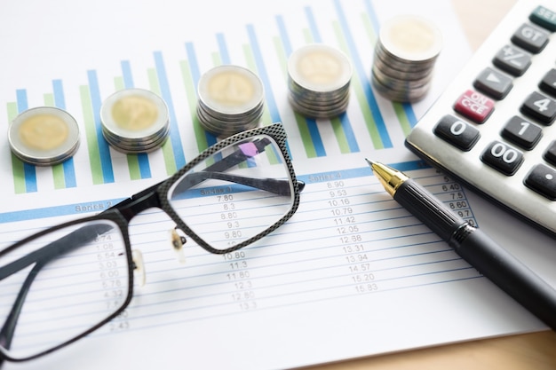 Finanzielle Charts auf dem Tisch mit Laptop, Taschenrechner, Stift und Gläser Business-Konzept